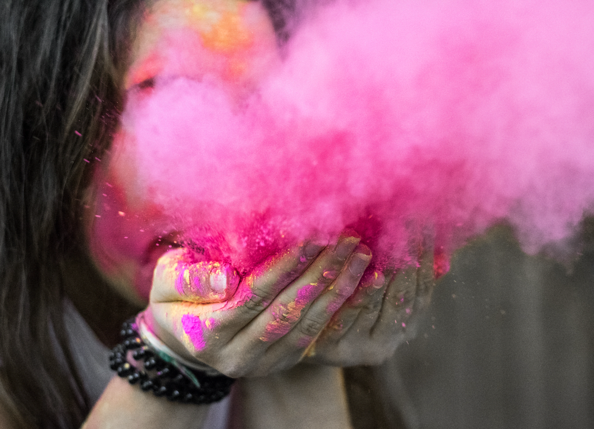 Young woman blowing pink powder from her hands