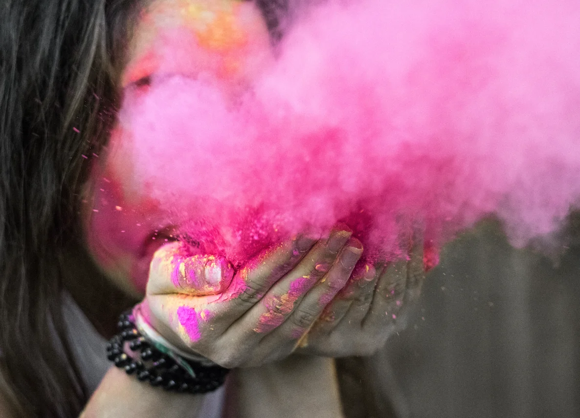 Young woman blowing pink powder from her hands